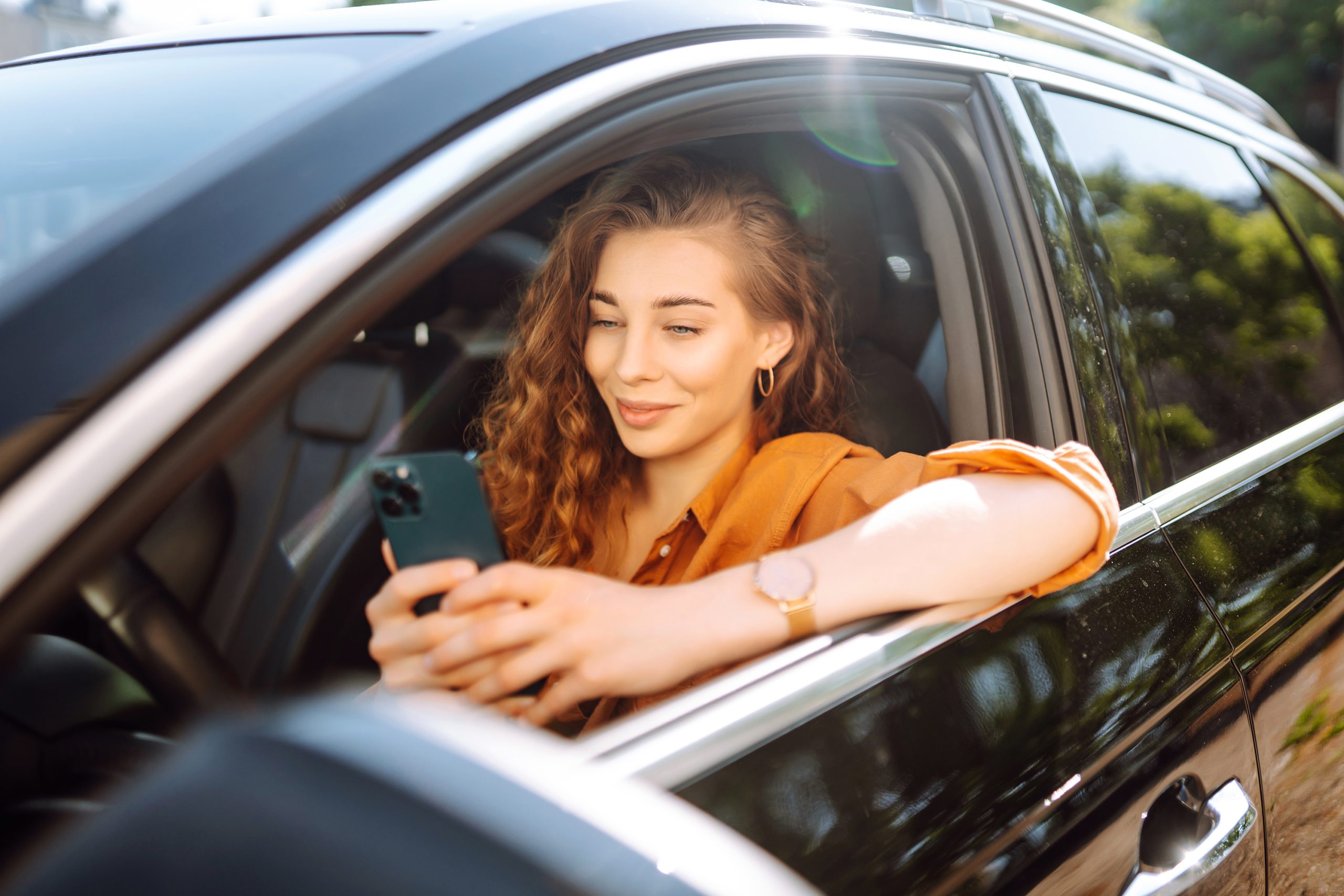 Beautiful woman driver in a car with a phone in her hands. The driver of the car uses a smartphone. Leisure, travel, technology, navigation.